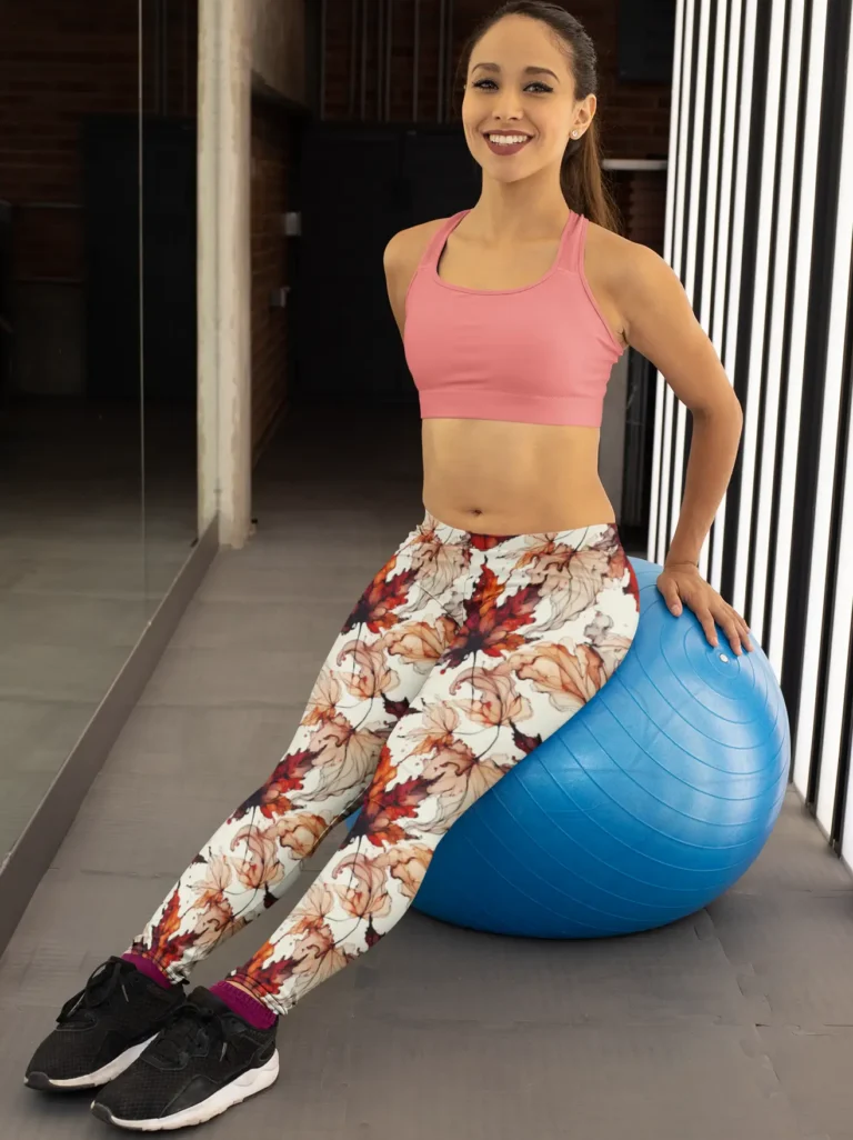 Woman wearing NCharnt Trendy yoga leggings Red and orange Maple leaf on white background sitting on exercise ball