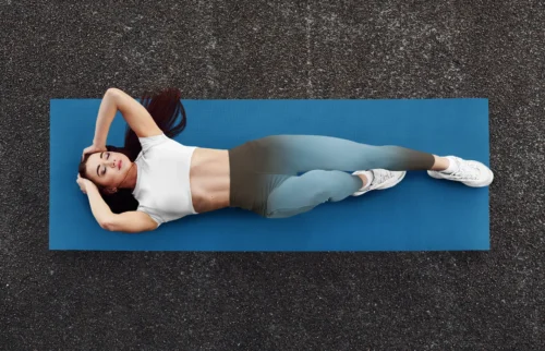 Woman in NCharnt sculpting athletic leggings in blue and brown gradient lying on a yoga mat Woman in NCharnt sculpting athletic leggings in blue and brown gradient lying on a yoga mat